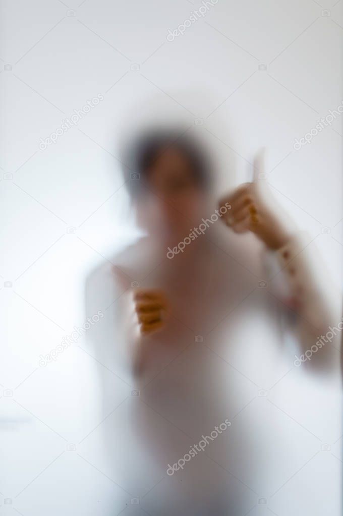 Blurry figure of a woman with thumbs up behind frosted glass