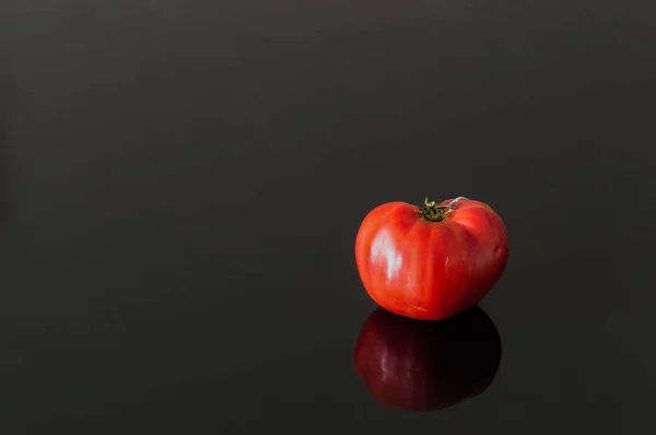 Un tomate orgánico grande sobre un fondo negro — Foto de Stock