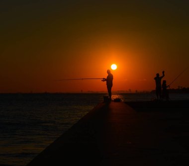 Gün batımında deniz balıkçıların siluetleri