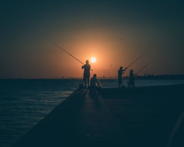 Gün batımında deniz balıkçıların siluetleri