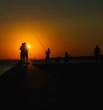 Gün batımında deniz balıkçıların siluetleri