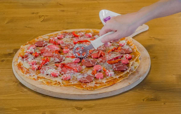 Kaukaski kobieta ręcznie cięcia krepy pizza z kiełbasą, papryka i serem na płycie — Zdjęcie stockowe