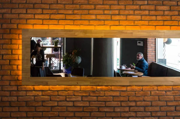 Reflektierte Ansicht eines Cafés und Kunden in einem Spiegel an einer Ziegelwand — Stockfoto