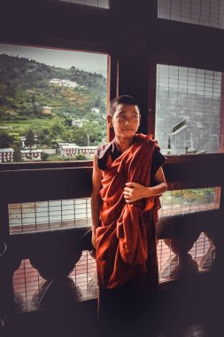 Thimphu, Bhutan - 10 Eylül 2016: Genç acemi Budist rahip pencerenin içinde bir manastır önünde kırmızımsı turuncu elbiseler duran.