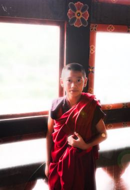 Punakha, Birleşik Arap Emirlikleri - 10 Eylül 2016: Genç acemi Budist rahip pencerenin içinde bir manastır önünde kırmızımsı turuncu elbiseler duran.