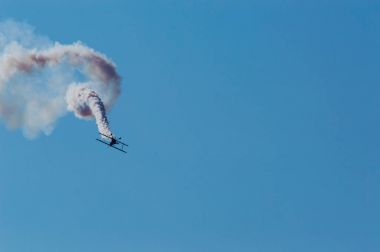 Akrobasi uçağı mavi gökyüzünde bir beyaz duman iz bırakarak.