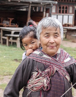 Bumthang, Bhutan - 14 Eylül 2016: bir çocuk Bumthang Valley, Bhutan sırtında taşıyan Bhutan yaşlı kadın.