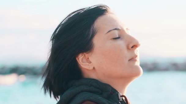 Profile of a natural brunette woman with no makeup enjoying the breeze and the sunshine with eyes closed near the sea. — Stock Video