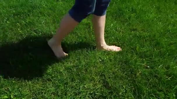 Vista laterale di gambe di donna in collant blu che camminano lentamente a piedi nudi su erba verde in un parco — Video Stock