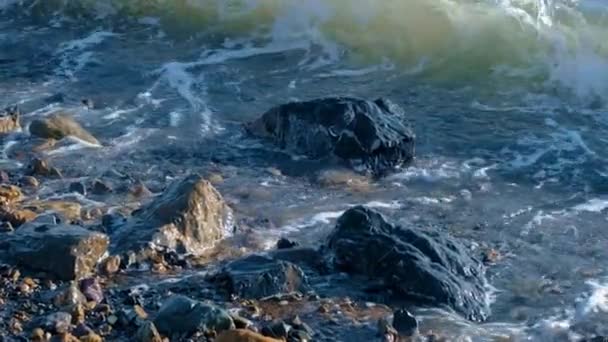 Powolny ruch fale morskie z białą pianką myjącą kamienie żwirowe i skały na plaży — Wideo stockowe