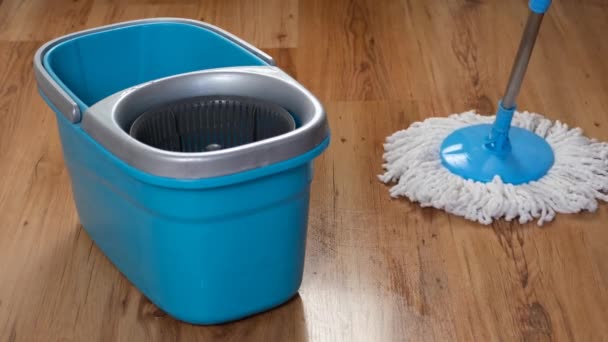 Vista frontale di un secchio blu e uno straccio bagnato piatto che pulisce lentamente il parquet nel soggiorno — Video Stock