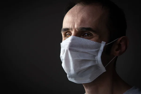 Adult man wearing hygienic mask to prevent infection, airborne respiratory illness such as flu, 2019-nCoV on dark background. Healthcare concept.