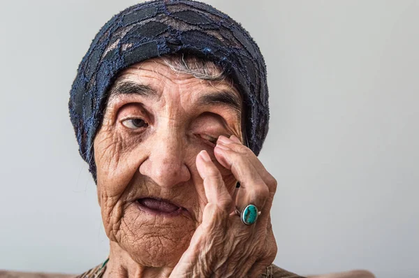 Portrait of an elderly Turkish woman with traditional bonnet rubbing eye on white background.