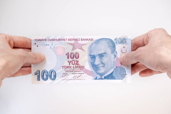 Female hand holding a 100 Turkish Lira (TRY) banknote isolated on white background.