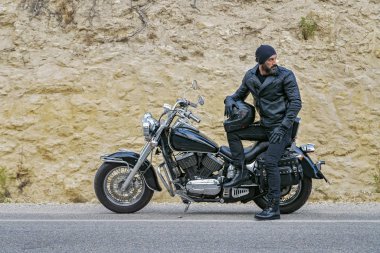 Adamın biri asfalt yolda motosiklet park etmiş..