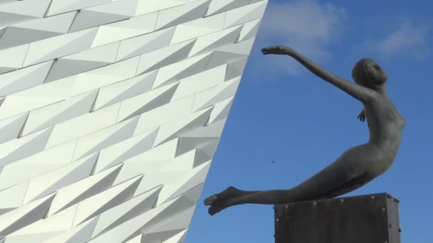 Скульптура женщины возле фасада музея "Титаник" в Белфасте, здание центра для посетителей и туристическая достопримечательность — стоковое видео