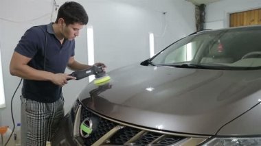 Oto yıkama makinesiyle araba cilalayan bir adam.