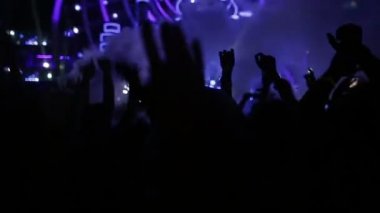 Parlak sahne ışıkları önünde konser kalabalığının siluetleri