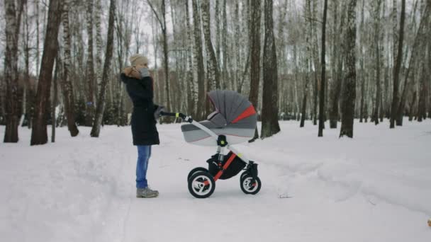 Bir bebek arabası ile yürüyen genç bir anne yan görünüm — Stok video