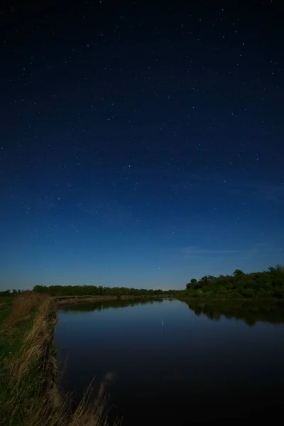 The stars in the night sky are reflected in the river. The lands