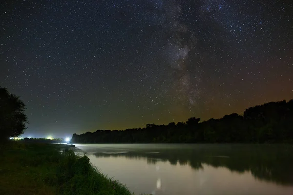 Milky Way stars in the sky above the river. Night landscape photographed with a long exposure.