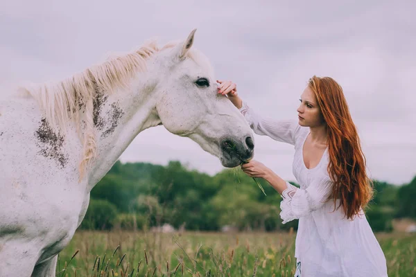Roodharige vrouw voeding paard — Stockfoto