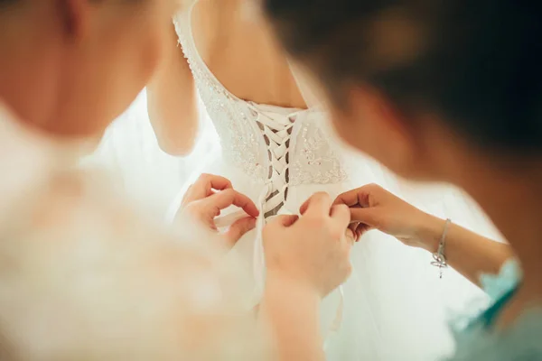 bridesmaids helping lacing up dress