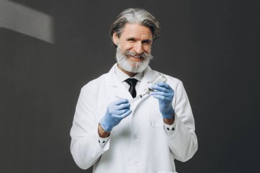 Eldivenli ve tıbbi maskeli yaşlı erkek doktor elinde şırınga tutuyor..