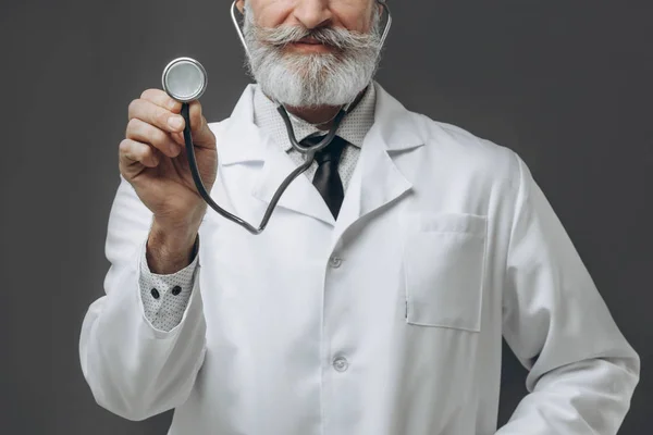 Médico sénior segurando um estetoscópio em sua mão estendida . — Fotografia de Stock