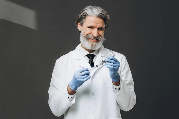 Ο ηλικιωμένος άνδρας γιατρός με γάντια και ιατρική μάσκα κρατάει τη σύριγγα.. — Φωτογραφία Αρχείου
