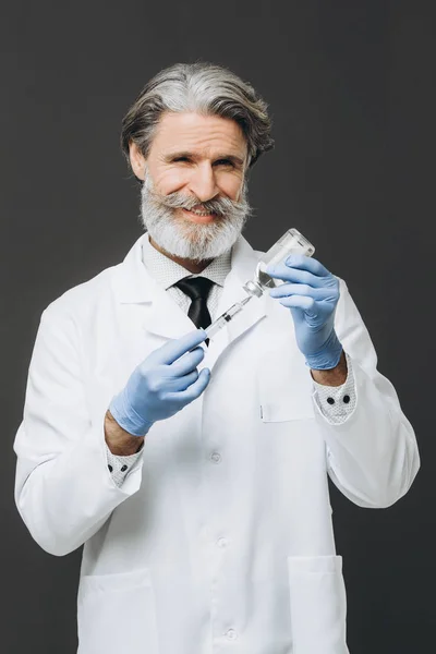 Η σύριγγα με το φάρμακο στα χέρια ενός ηλικιωμένου, χαμογελαστού γιατρού. — Φωτογραφία Αρχείου