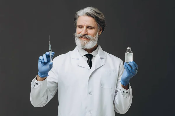 Η σύριγγα με το φάρμακο στα χέρια ενός ηλικιωμένου, χαμογελαστού γιατρού. — Φωτογραφία Αρχείου