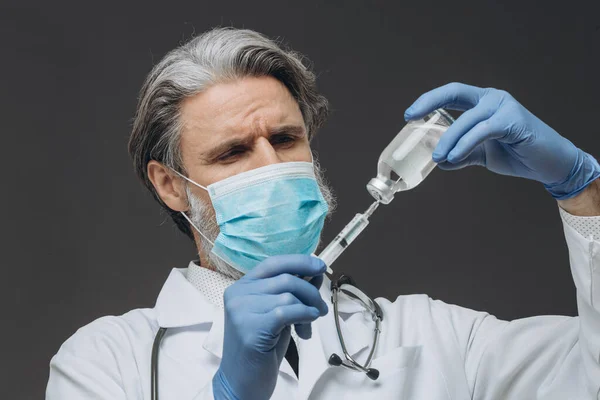 Velho médico em luvas e máscara médica está segurando seringa . — Fotografia de Stock