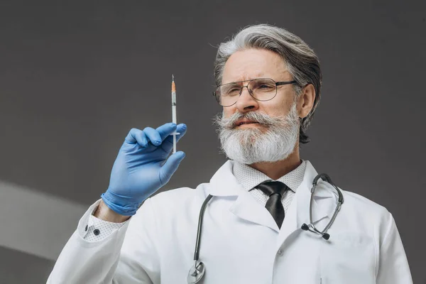 Old serious doctor holding syringe with vaccine. Ready to make injection.