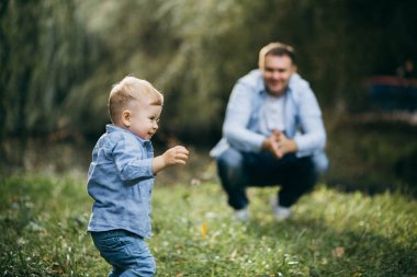 Mutlu genç aile deniz kenarında yeşil doğada birlikte vakit geçiriyor. Ebeveynler dışarıda çocuklarla oynuyor. Aile gün batımında yürüyor, sarılıyor ve eğleniyor.