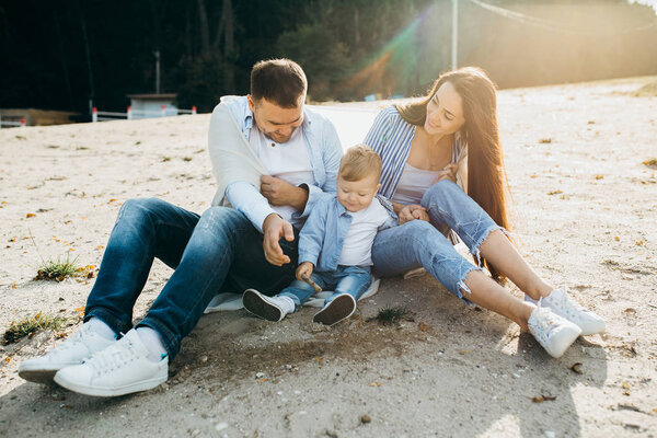 Beautiful happy family sitting on the coast, while walking near the lake on a spring day.