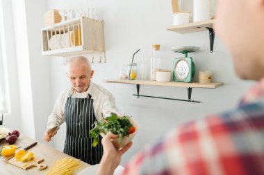 Genç adam ve babası mutfakta yemek pişiriyor.