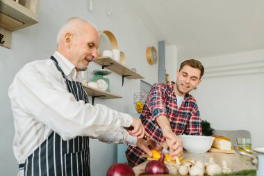 Genç adam ve babası mutfakta yemek pişiriyor.