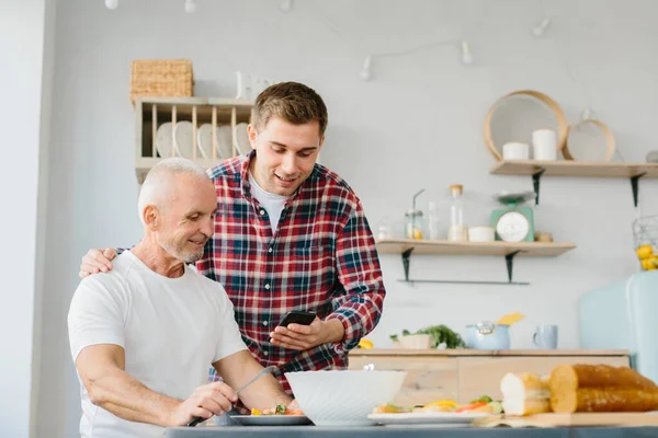 台所で電話を使用して若い男と高齢者の父親 — ストック写真