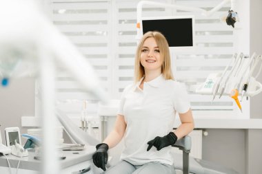 Kadın dişçinin portresi. Ofisinde duruyor ve güzel bir gülümsemesi var..