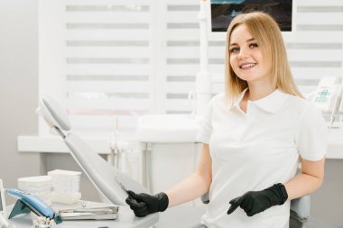 Kadın dişçinin portresi. Ofisinde duruyor ve güzel bir gülümsemesi var..