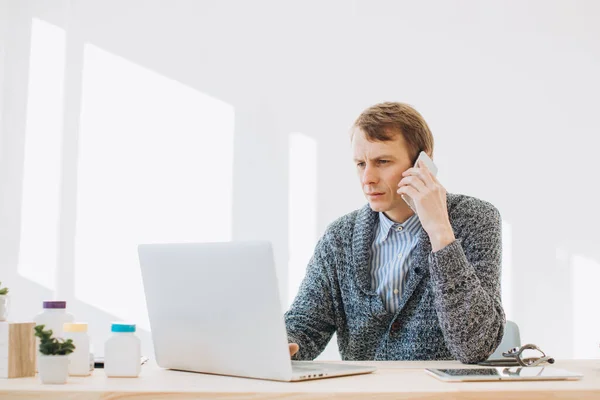 A young man, a manager of a pharmaceutical company, talks on the phone in his office.