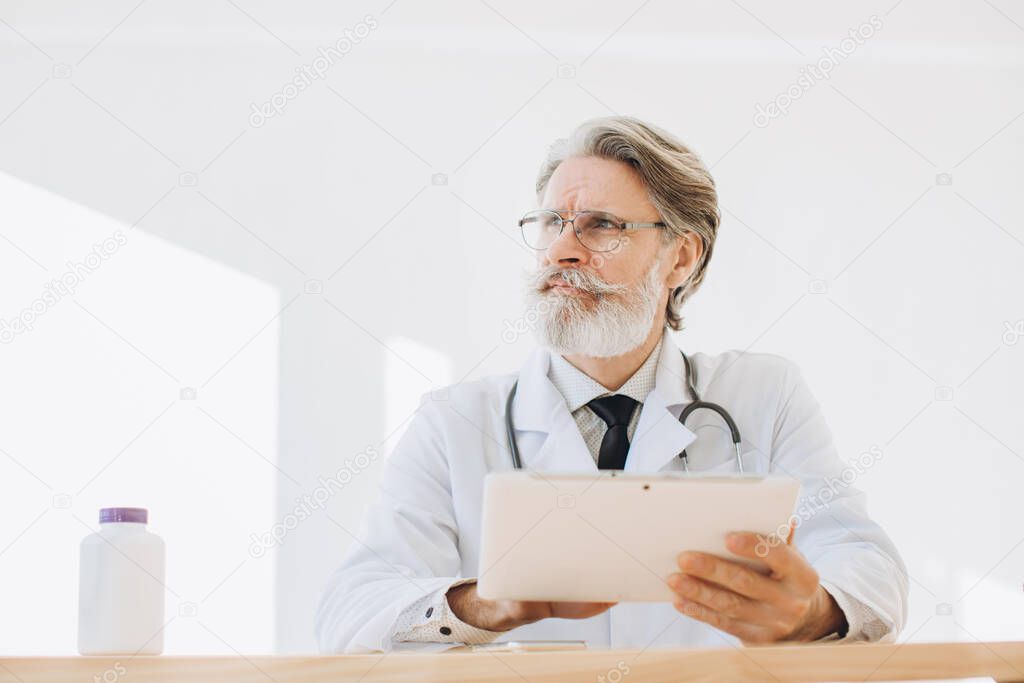 Portrait of senior doctor using application on tablet computer