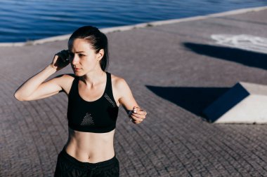 Siyah giyinmiş genç kız sabah koşusu sırasında kulaklıkla müzik dinliyor..