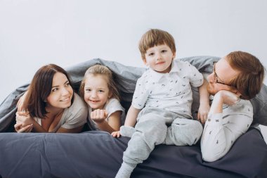 Çocuklu genç ebeveynler hafta sonları yatakta eğleniyor..