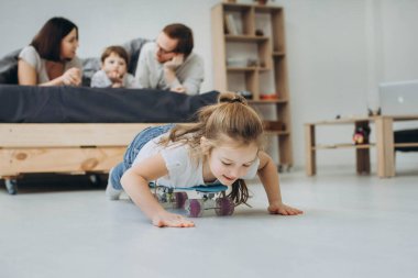 Okul öncesi çocukların olduğu bir aile odada paten oynuyor..