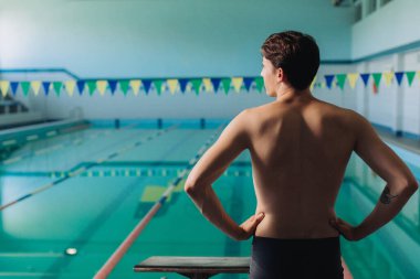 Siyah mayo giymiş erkek yüzme hocası havuzda poz veriyor.