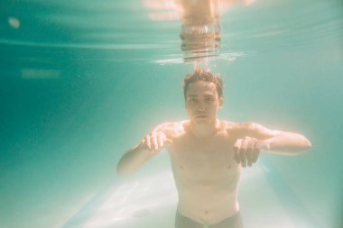 Siyah şortlu erkek eğitmen suyun altında yüzüyor.