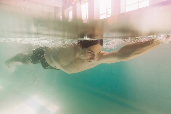 Male instructor in black swimming trunks is swimming under water