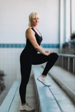 Spor merkezinde poz veren siyah eşofmanlı sarışın yüzme hocası.